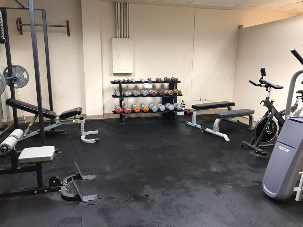 The Canyon employee recreation center at Yellowstone features weight benches, a rack of dumbbells, an exercise bike, weightlifting equipment, and black rubber flooring.