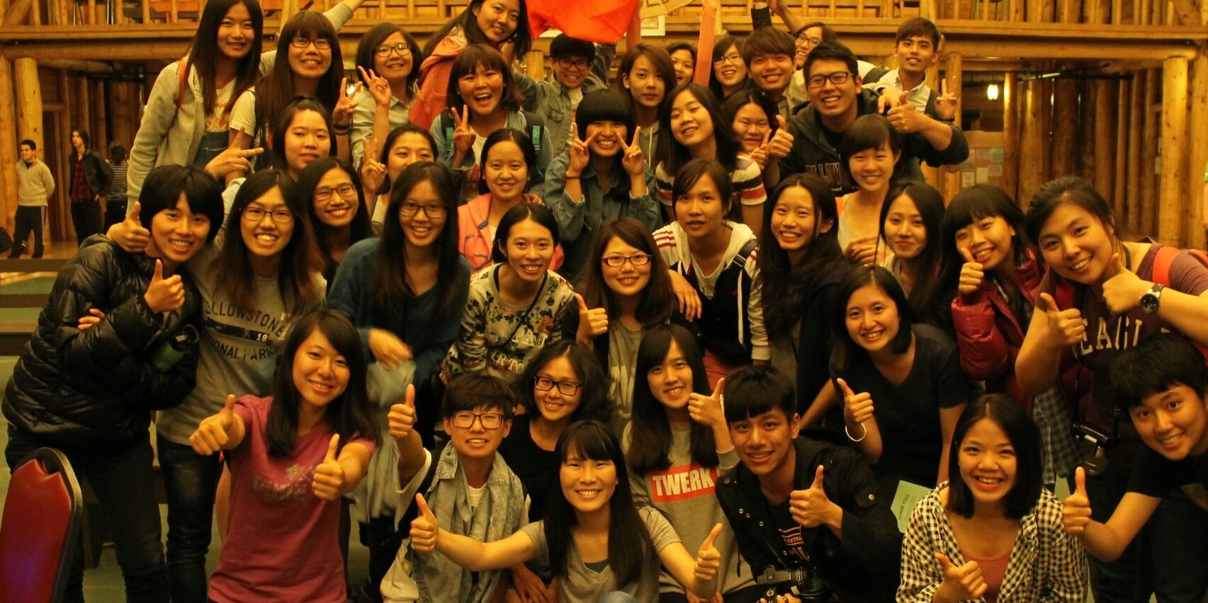 A large group of young people poses indoors, many giving thumbs up, with one person in the back holding a Taiwanese flag—capturing the spirit of the Yellowstone employee recreation program.